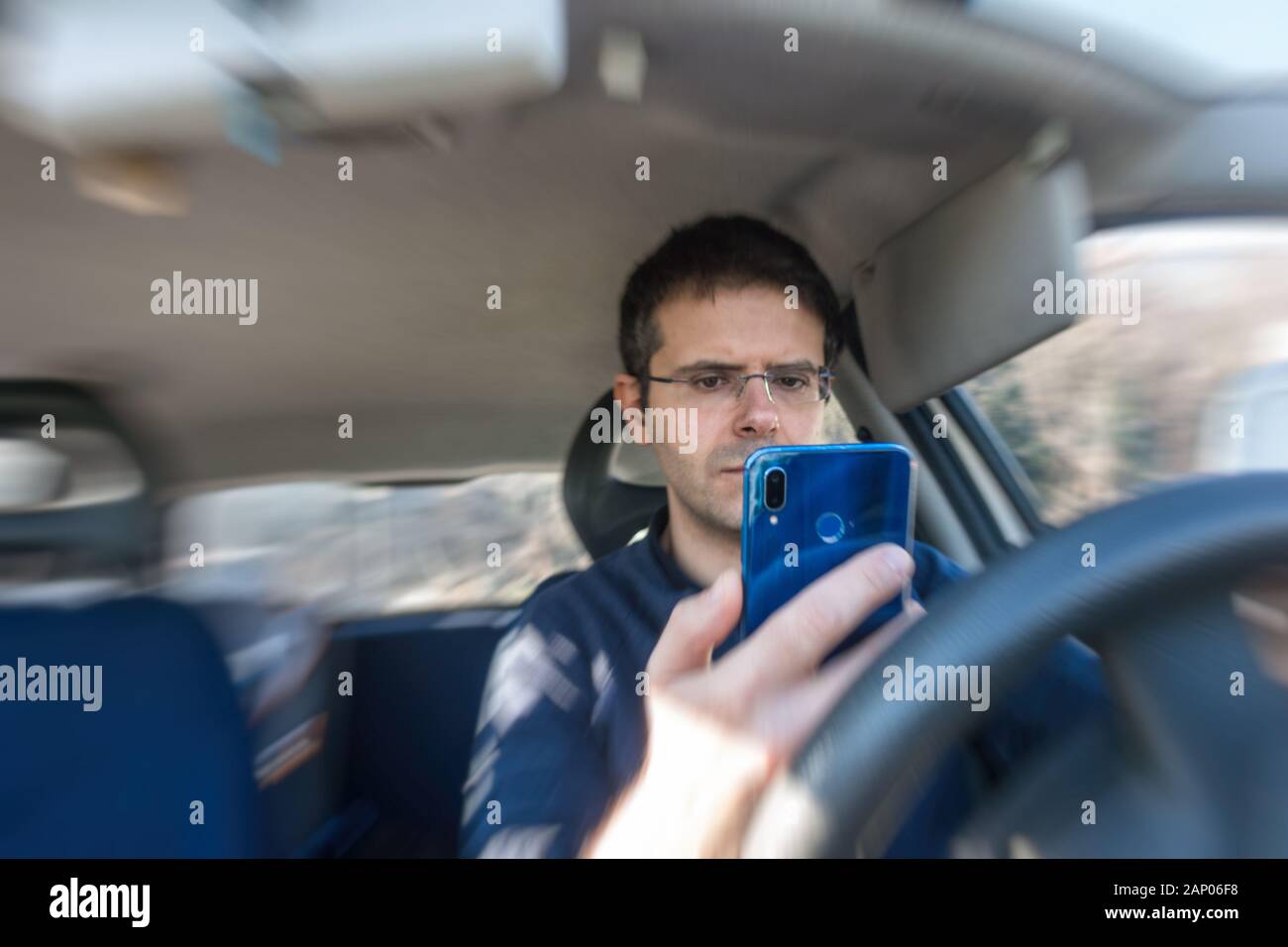 L'uomo utilizza smartphone durante la guida in auto. La guida pericolosa e comportamento inconscio concetto. Foto Stock