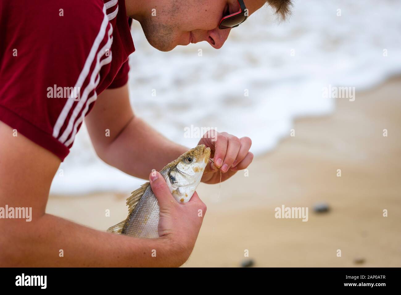 Un mare pescatore sgancia un pesce prima di restituirlo al mare. Foto Stock