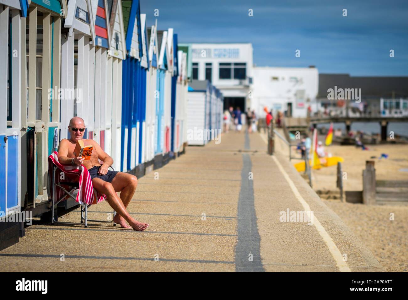 Un uomo seduto in una sedia pieghevole al sole a leggere un libro sul mare. Foto Stock