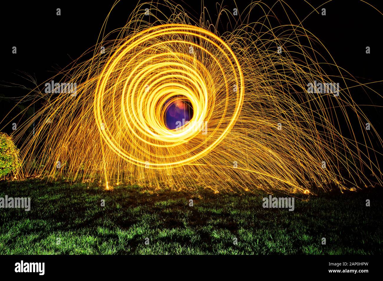 Fuochi d'artificio con motivo circolare realizzati girando la lana di filo in fiamme in una frusta all'uovo che mostra sentieri leggeri e scintille volanti Foto Stock