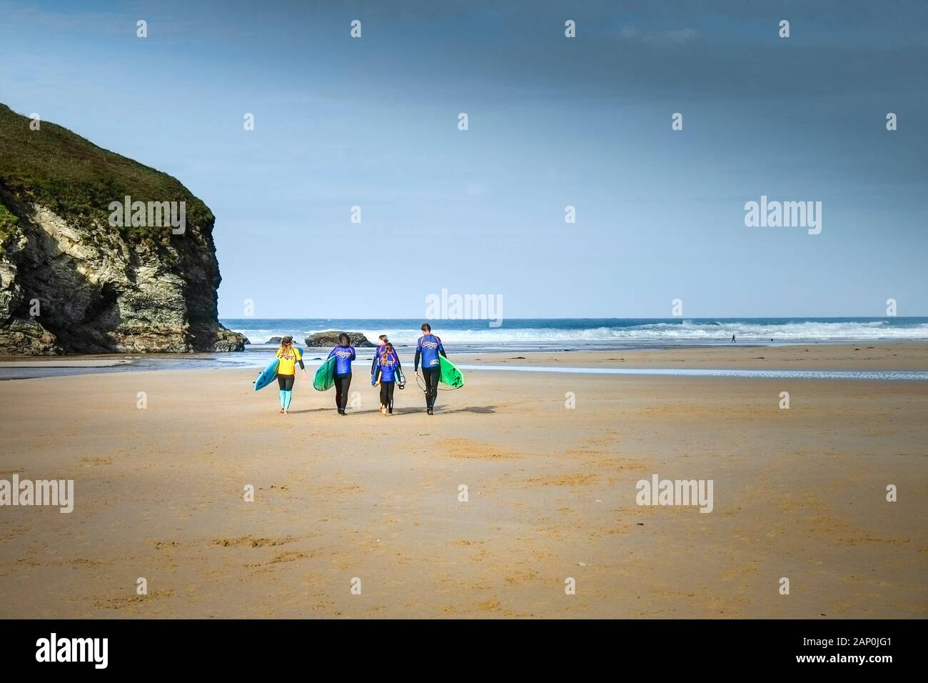 Un gruppo di surfers e loro istruttore che trasportano le loro tavole da surf su Mawgan Porth Beach a nord della costa della Cornovaglia. Foto Stock