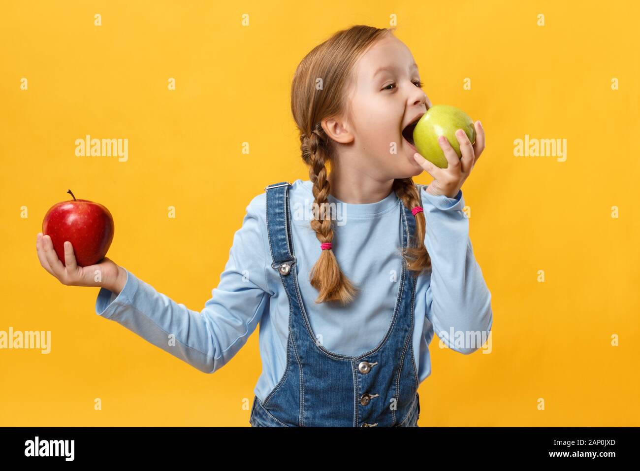 Mangiare sano concetto. Un bambino morde un apple. Bambina su uno sfondo giallo. Foto Stock