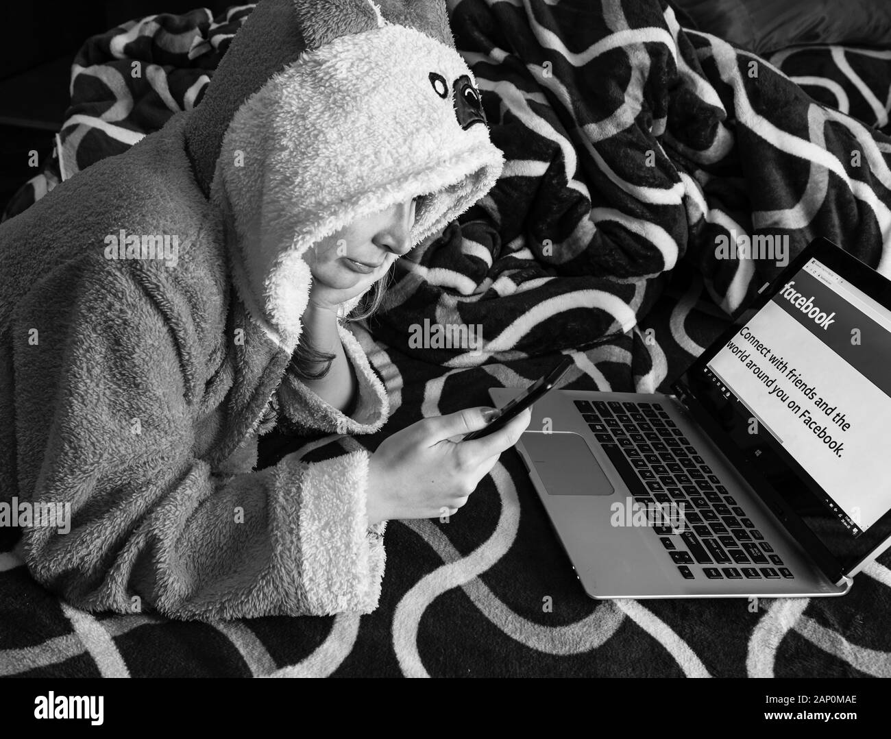 Donna che utilizza un computer portatile nel suo letto, a casa. Ragazza il login a Facebook alla ricerca di notizie, social media concetto. Bucarest, Romania, 2020. Foto Stock