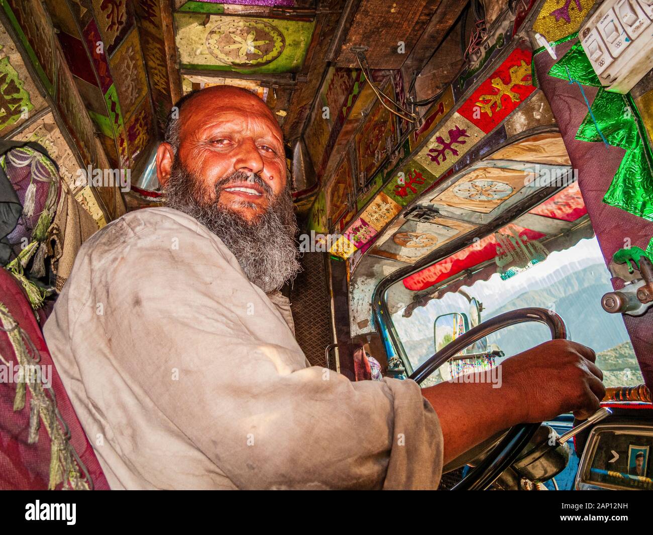 Vista all'interno della cabina di un camion colorato decorato e dipinto, guida sulle strade polverose della Karakorum Highway, conducente all'interno Foto Stock
