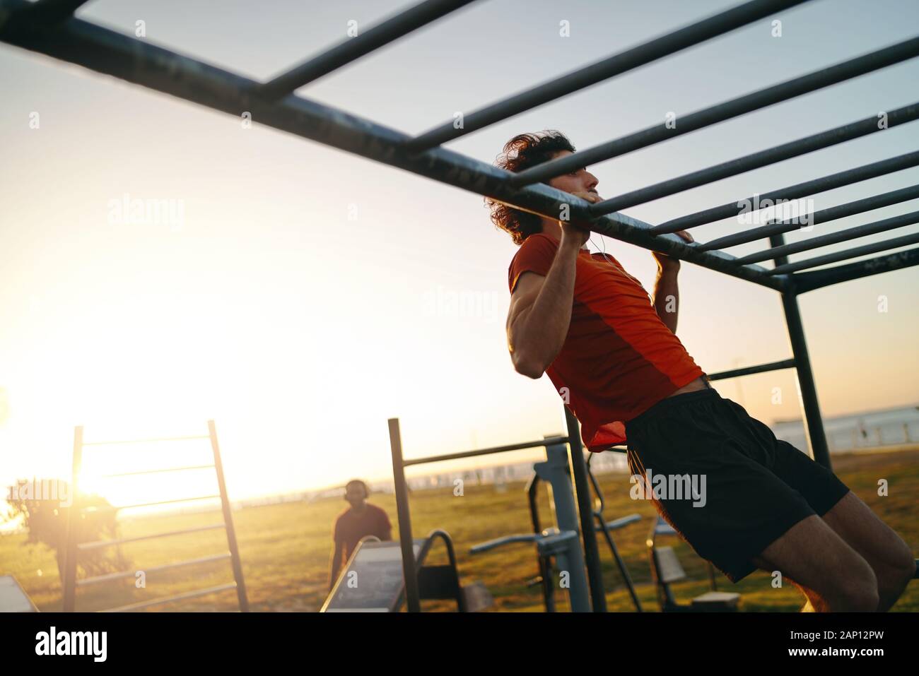Montare il giovane uomo che fa del pull-up in una palestra a cielo aperto parcheggio durante la luminosa calda giornata estiva Foto Stock