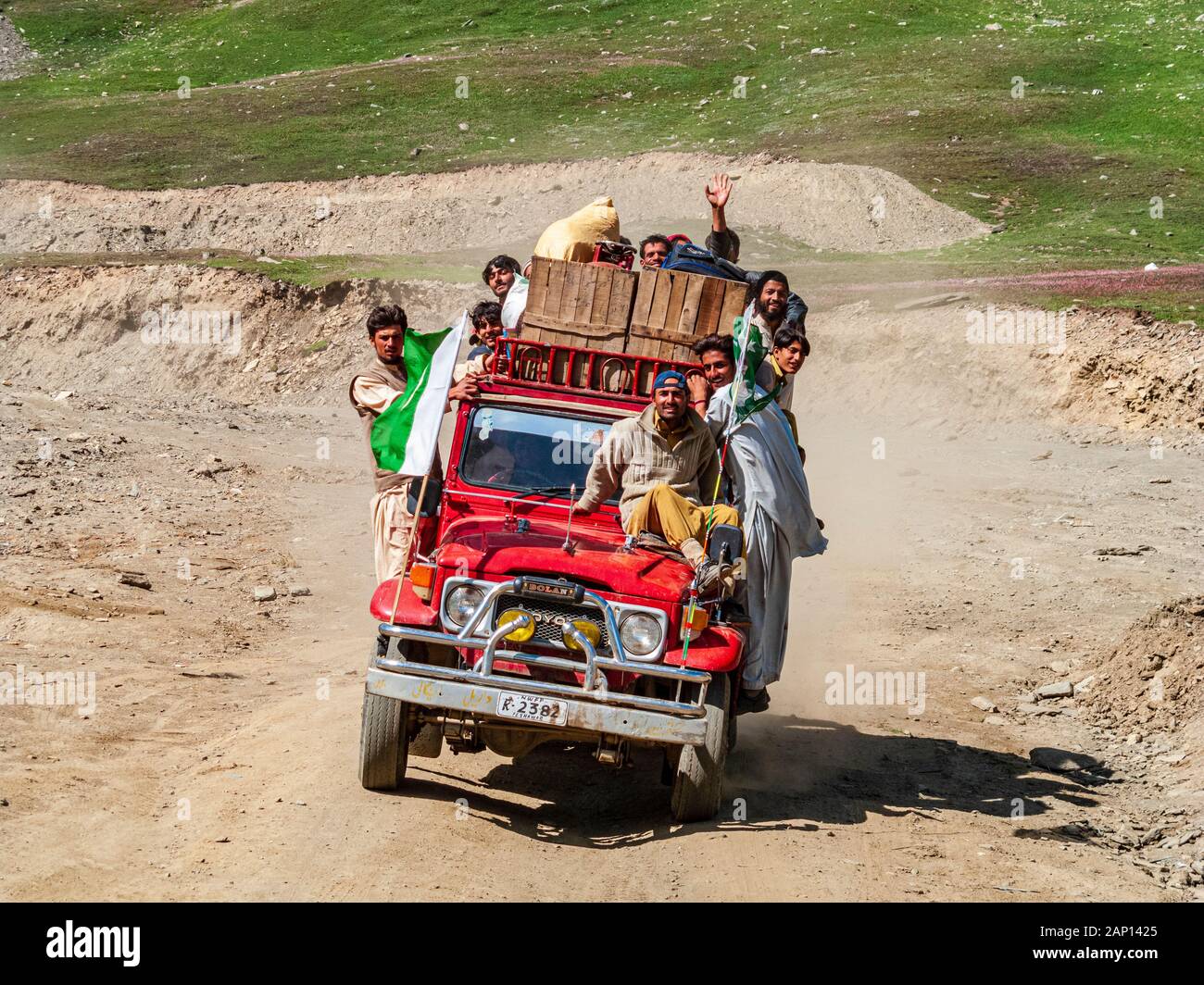 Le persone sono aggrappate a una jeep sovraccarica, guidando sulla strada polverosa fino al passo Babusar Foto Stock