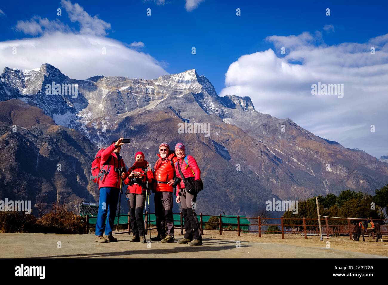 Quattro escursionisti in giacca invernale rossa stanno facendo selfie in Everest base Camp trekking con cielo blu e catena montuosa himalayana sullo sfondo Foto Stock