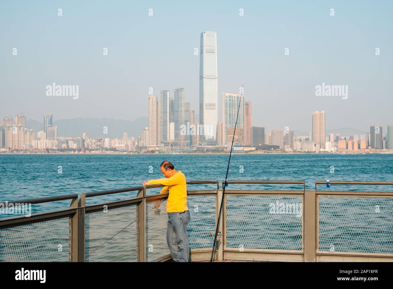 Hong Kong Cina - Novembre 2019: Fisher uomo con canna da pesca sulla costa con lo skyline di Hong Kong in background Foto Stock