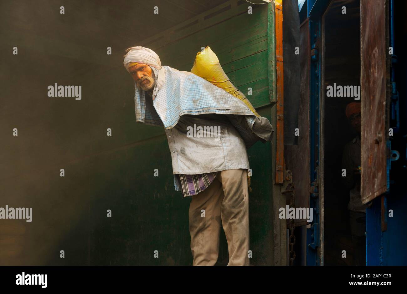 L'uomo lavora per scaricare la borsa di cemento in condizioni polverose dal treno in caldo estate in Mathura, India. Foto Stock