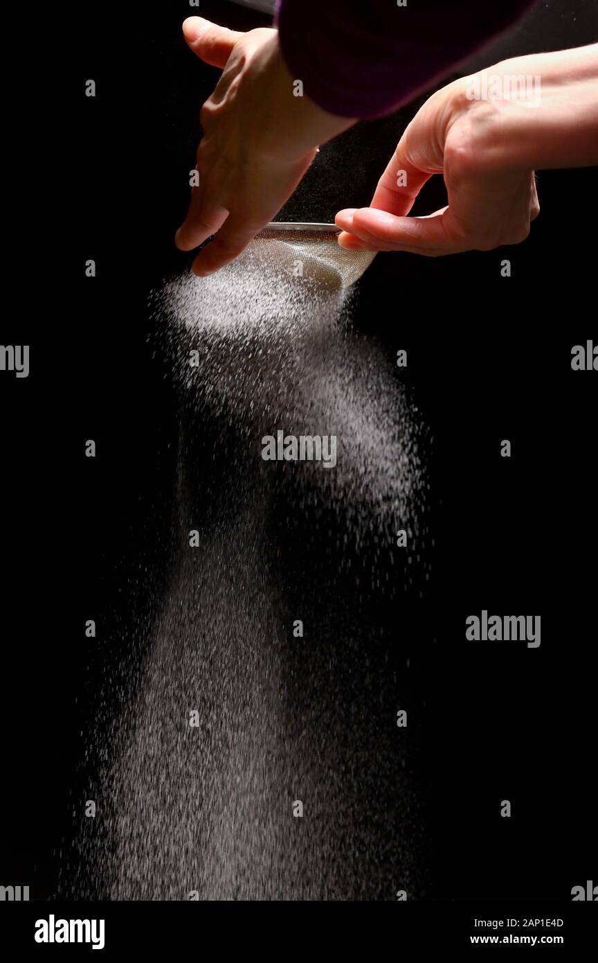 Polvere di zucchero Schizza da donna la mano su sfondo nero Foto Stock