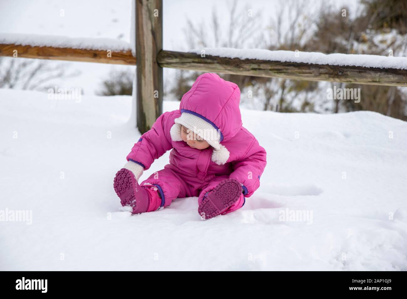 Baby girl in tuta rosa seduto in un campo di neve su un molto soleggiata  giornata invernale Foto stock - Alamy