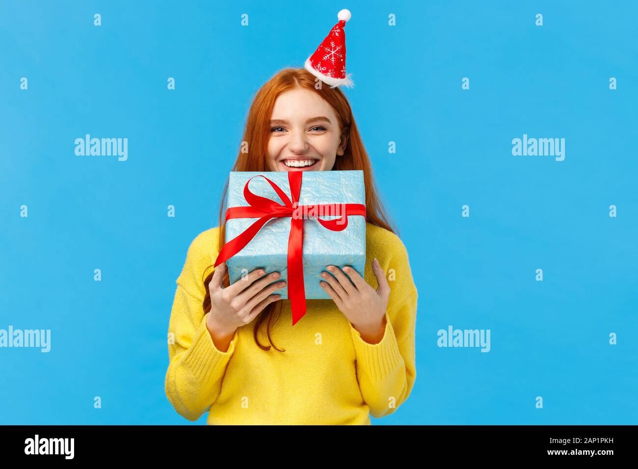 Ragazza cant attendere dare fratello del suo regalo, sorridere portare carino natale avvolto presente e indossare elegante santa cappello, ridere, condividere emozioni positive Foto Stock