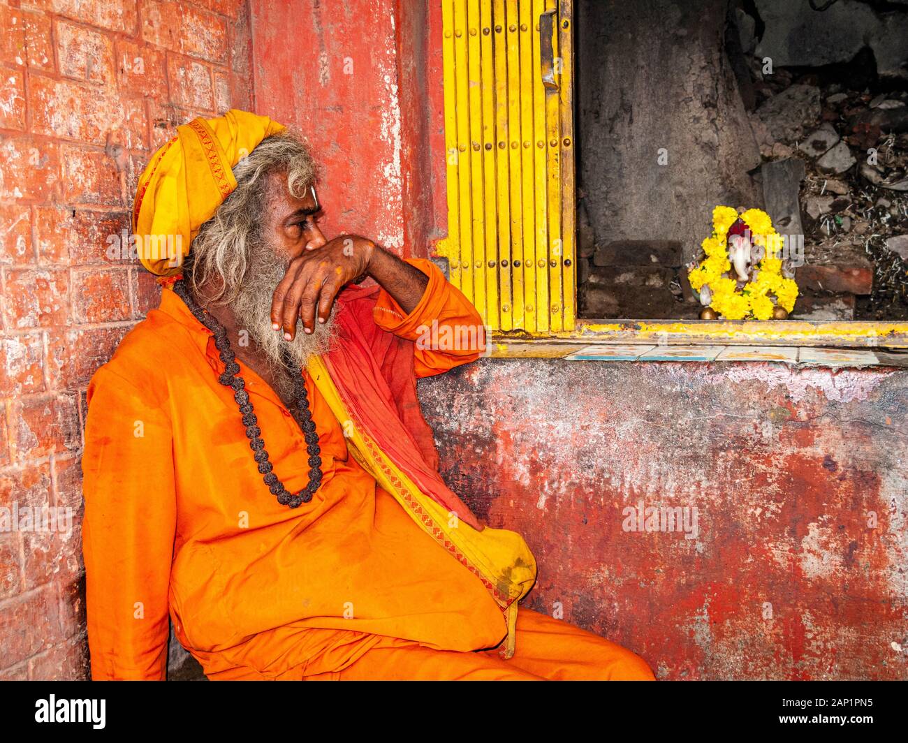 Un Sadhu, santo uomo, con panni d'arancia, seduto di fronte ad un piccolo santuario Foto Stock