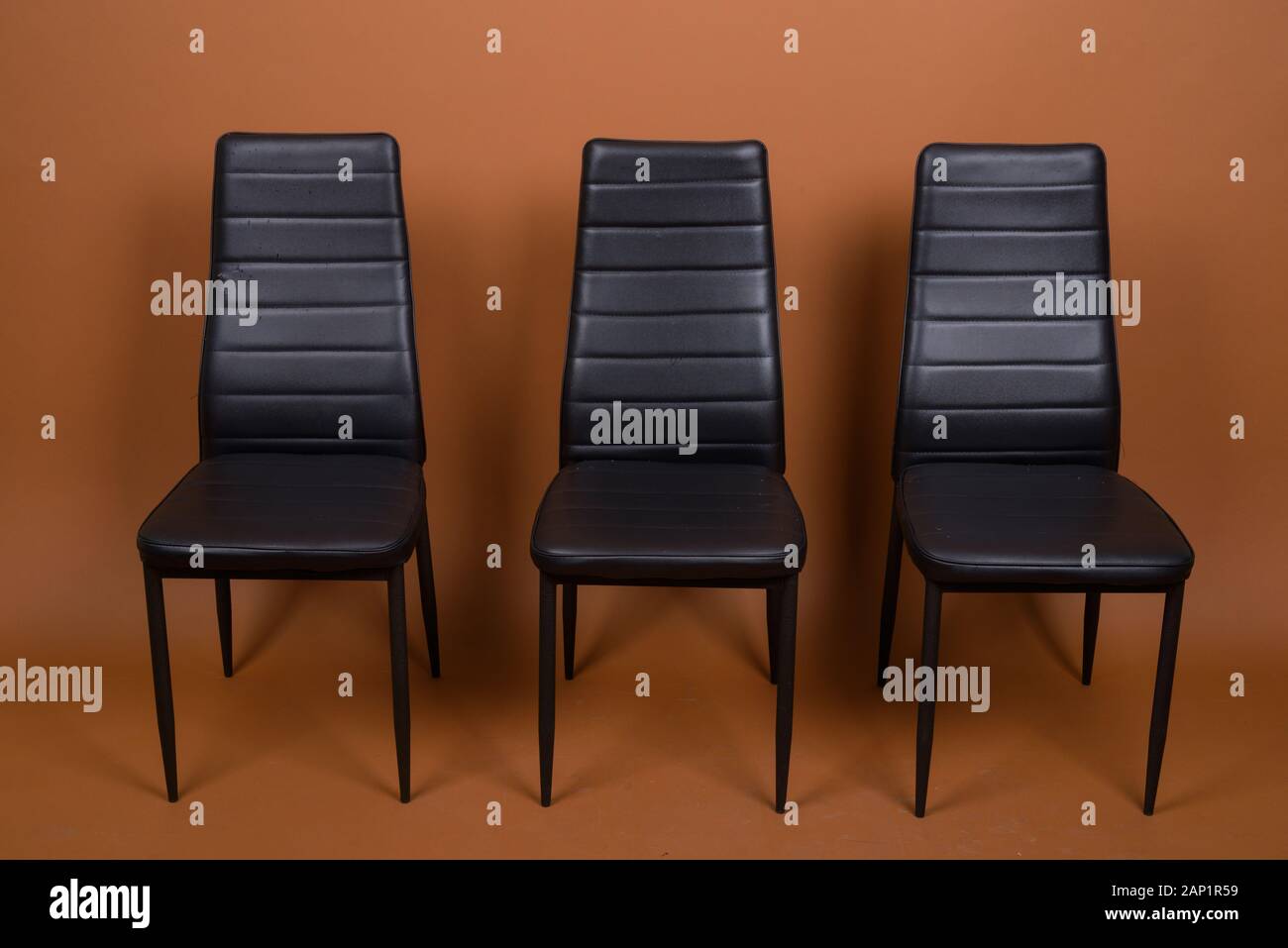 Tre sedie in pelle allineati contro sfondo marrone Foto Stock