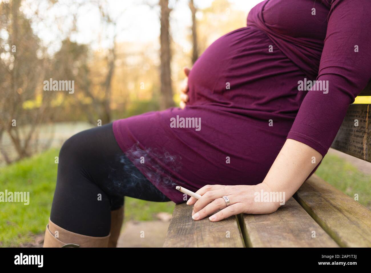Close-up sulla donna incinta con il fumo di sigarette in mano, seduti su una panchina nel parco. Le cattive abitudini durante la gravidanza e il rischio per la salute dei bambini Foto Stock