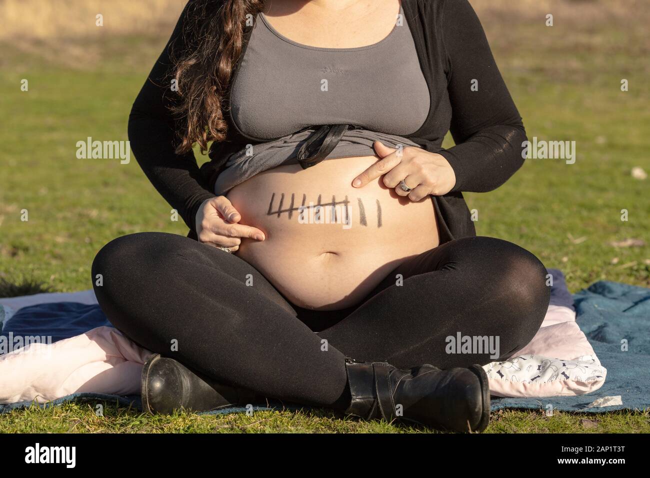 Donna incinta seduta sul terreno nel parco, puntando al suo ventre con sette mesi del termine marcatura disegno sulla pelle Foto Stock