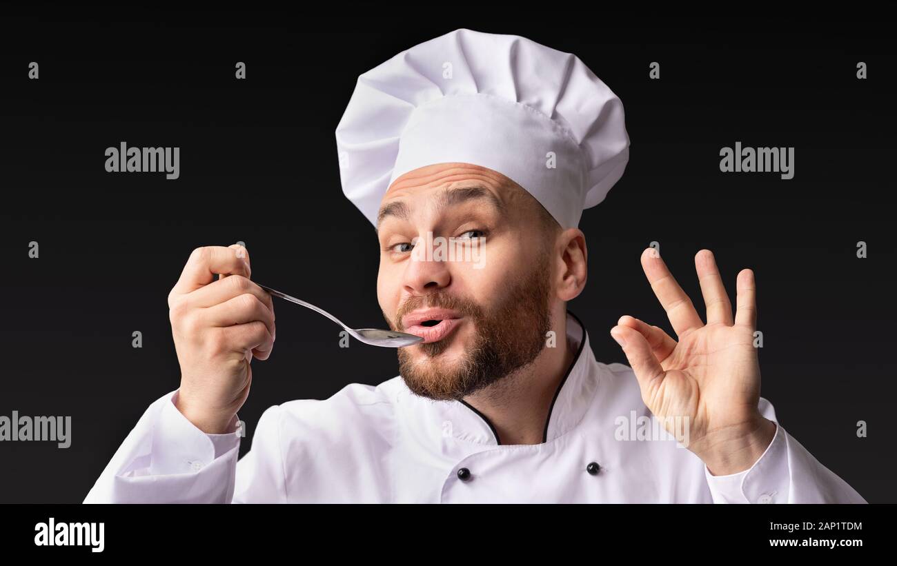Lo Chef degustazione e approvazione di cibo cucchiaio di contenimento in posa di Studio Foto Stock