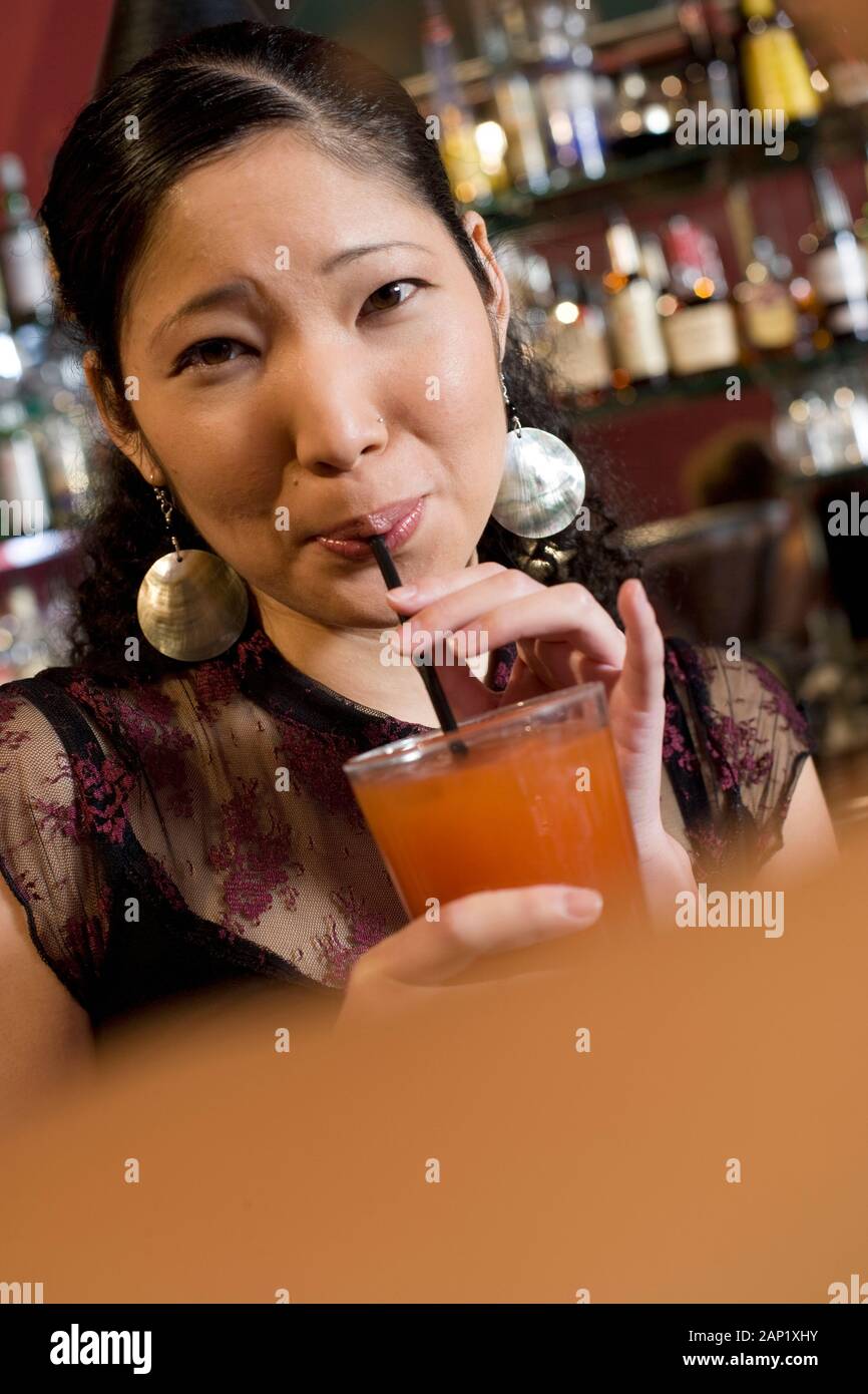 Giovane donna asiatica millenaria americana sorseggiando un drink in un bar locale Foto Stock