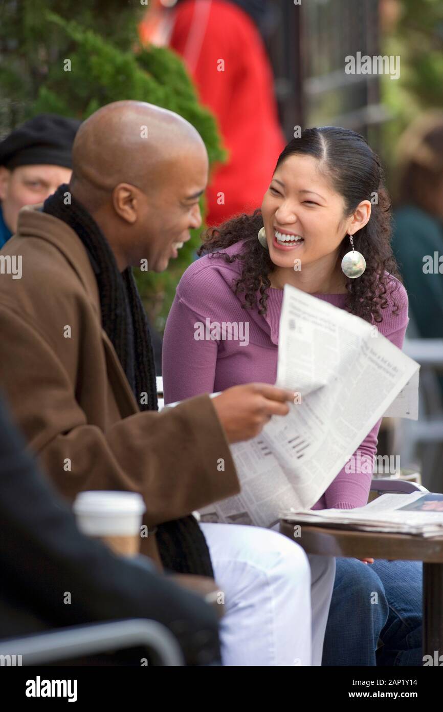 African American uomo e donna asiatica di leggere la carta in outdoor cafe Foto Stock