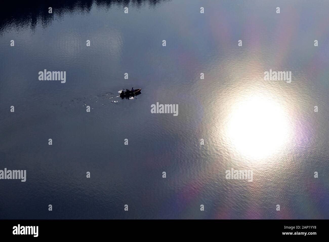 Una barca a remi in una bonaccia acqua di lago con sun riflessione. Foto Stock