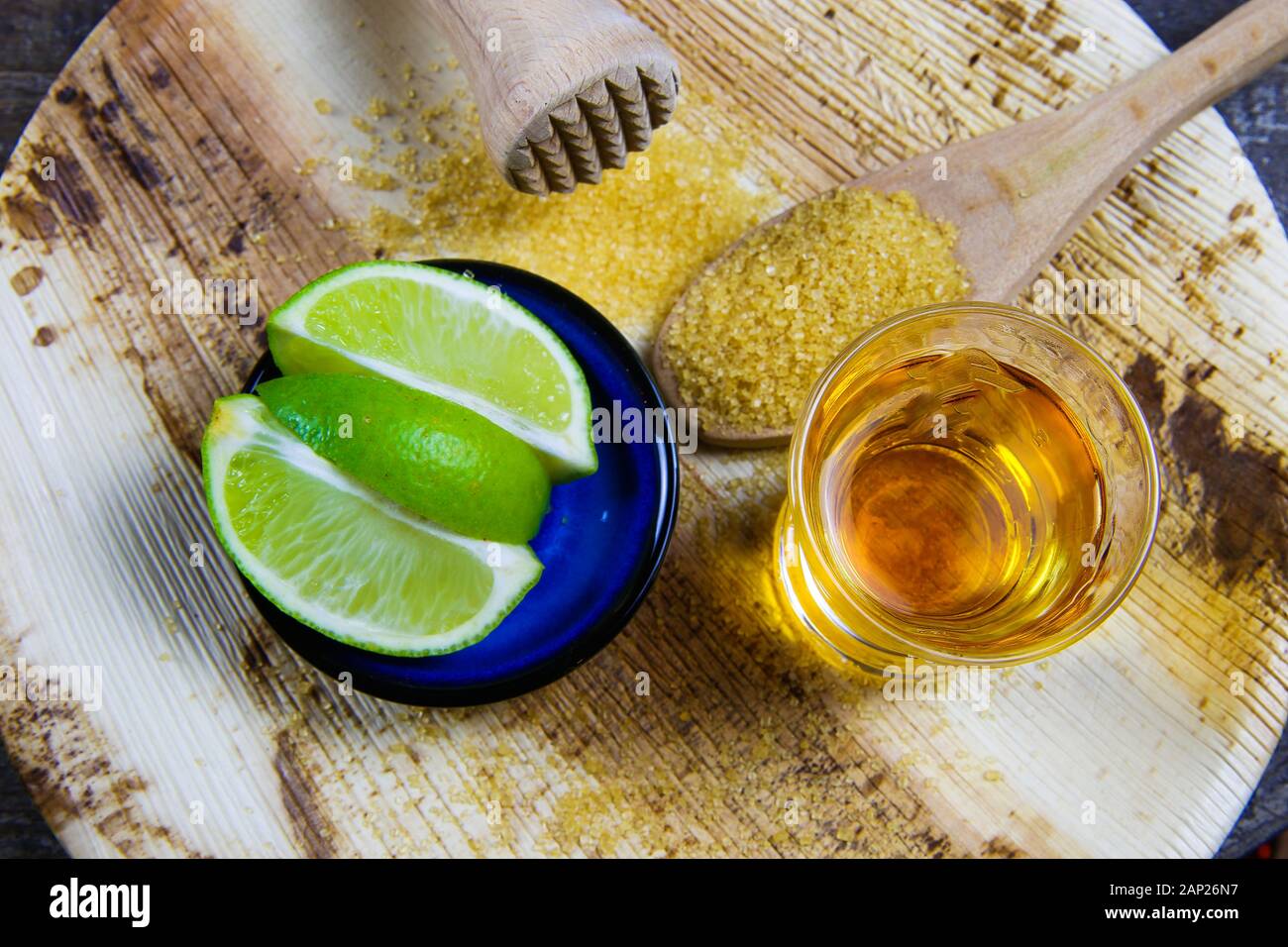Il ricevimento e la preparazione di caipirinha cocktail: Close up di vetro con cachaça, stantuffo in legno, fette di tigli e 1 cucchiaio di zucchero di canna Foto Stock