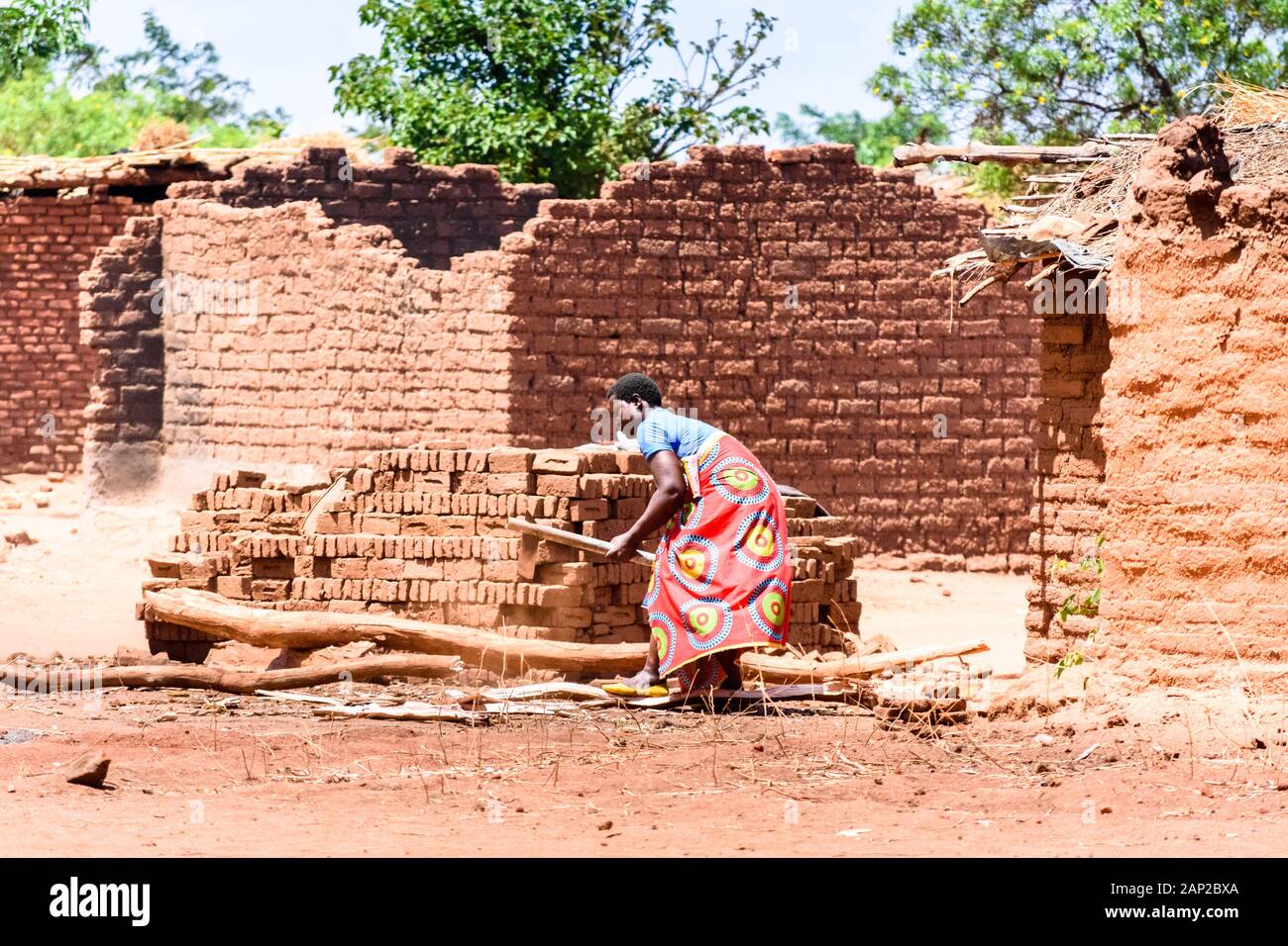 Malawia donna spacco legna da ardere con un'ascia da inserire in un vicino forno di mattoni in un villaggio Malawian Foto Stock