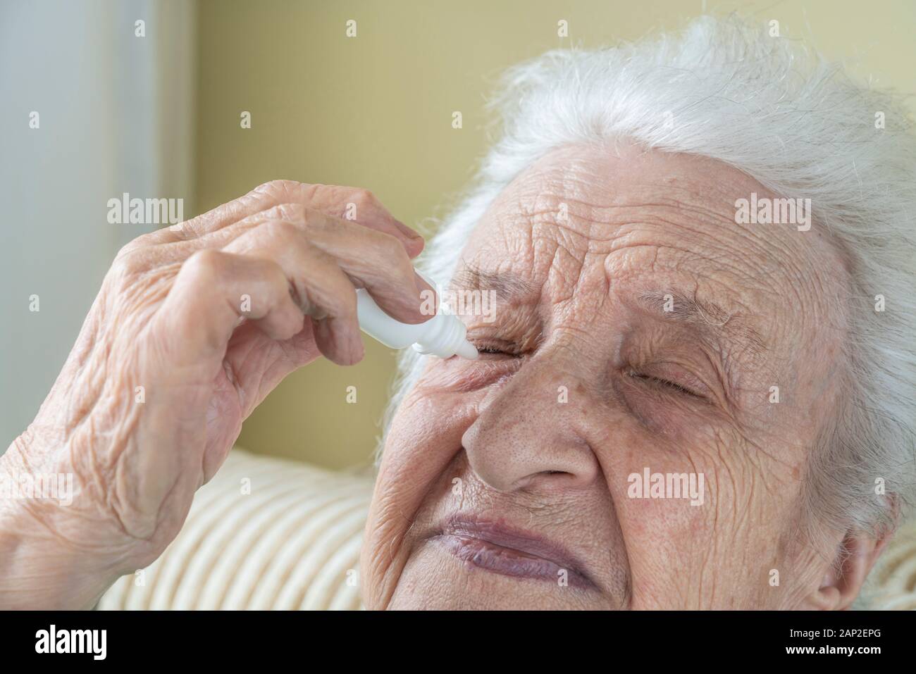 Un senior donna applicando gocce per gli occhi negli occhi da sé a casa Foto Stock