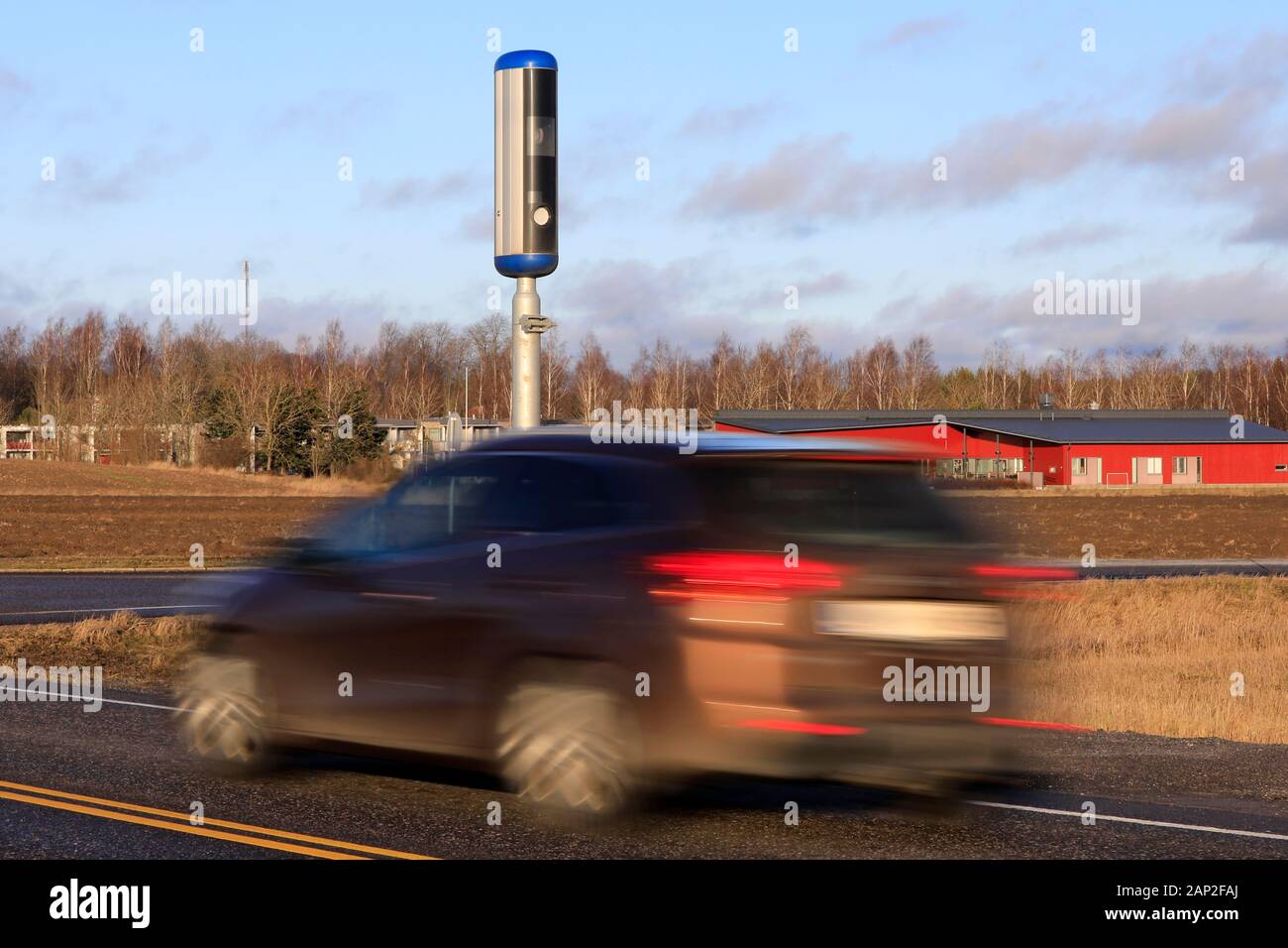 Auto passando una moderna strada fotocamera velocità entro il limite massimo di velocità su una giornata di sole d'inverno. Una lunga esposizione a sfumare il veicolo. Foto Stock