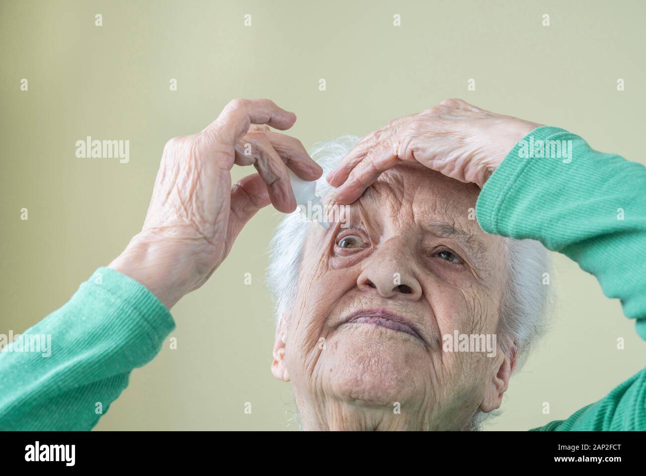 Un senior donna applicando gocce per gli occhi negli occhi da sé a casa Foto Stock