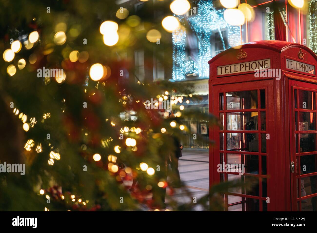 Tempo di Natale a Londra: un rosso cabina telefonica nella parte anteriore di un illuminato albero di Natale nel centro di Londra, Regno Unito, durante la notte Foto Stock