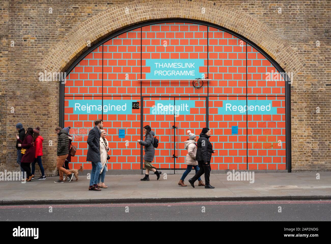 Le persone delle infrastrutture londinesi che passano davanti a un murale pubblicando il programma Thameslink alla stazione di London Bridge a Duke St Hill, Londra Regno Unito AS 2020 Foto Stock