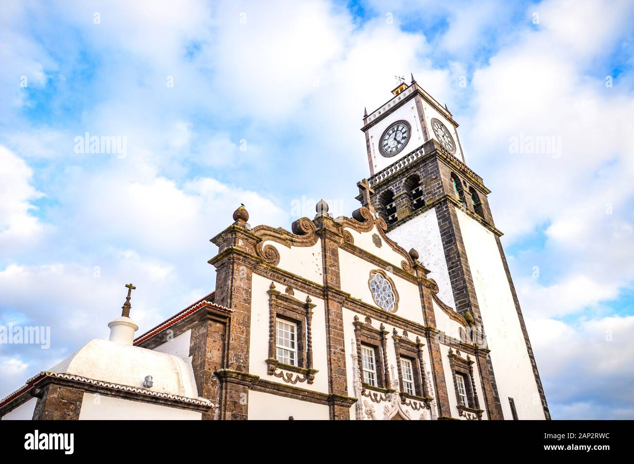 La facciata esterna di San Sebastian chiesa Igreja Matriz de Sao Sebastiao, a Ponta Delgada, Azzorre, Portogallo. White clock tower da sotto con il cielo blu e nuvole sopra. La luce del tramonto, ora d'oro. Foto Stock