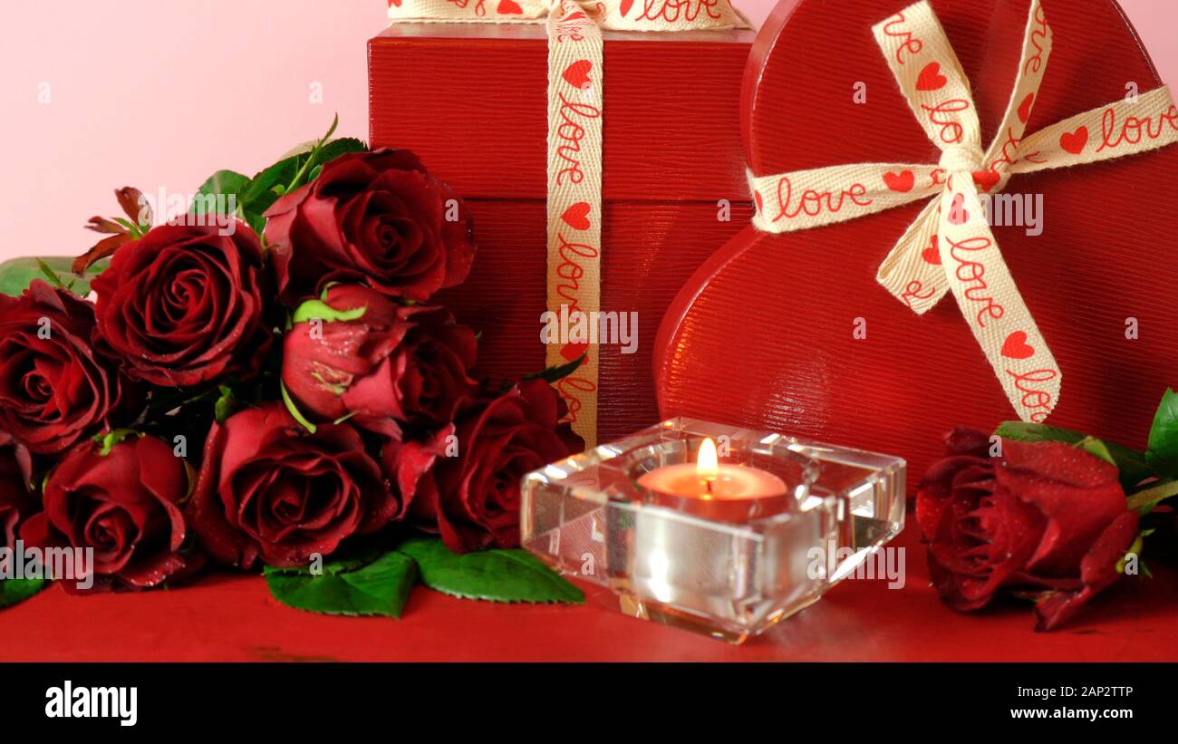 Happy regali di San Valentino e rose rosse sul rosso e sfondo rosa. In prossimità della messa a fuoco sulla candela accesa. Foto Stock