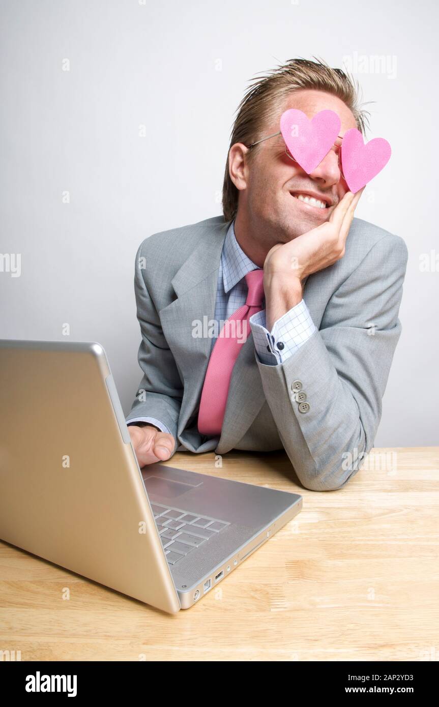 Felice lavoratore di ufficio digitazione sul suo computer portatile con cuori rosa svolazzanti oltre i suoi occhi Foto Stock
