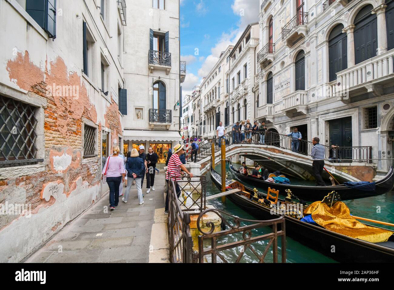 Una sezione di occupato di canal in Calle de la Canonica come turisti attraversare il ponte su una gondola e un gondoliere attende i clienti a Venezia, Italia Foto Stock