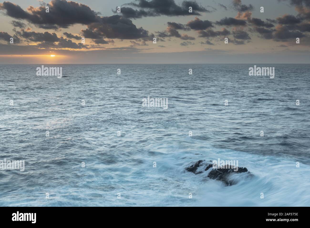 Soffice luce mattutina spazzolando la costa vulcanica del nord di Gran Canaria, dove l'Atlantico incontra rocce aspre e onde nebbiose in una costa tranquilla. Foto Stock