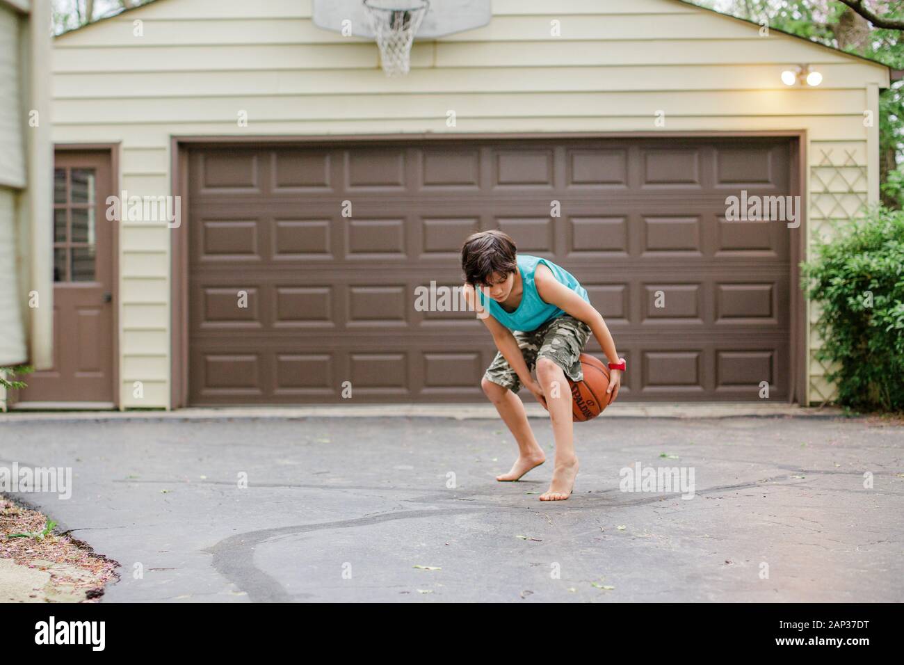 Un ragazzo a piedi nudi, il ragazzo di Tween si falla un basket nel suo vialetto al crepuscolo Foto Stock