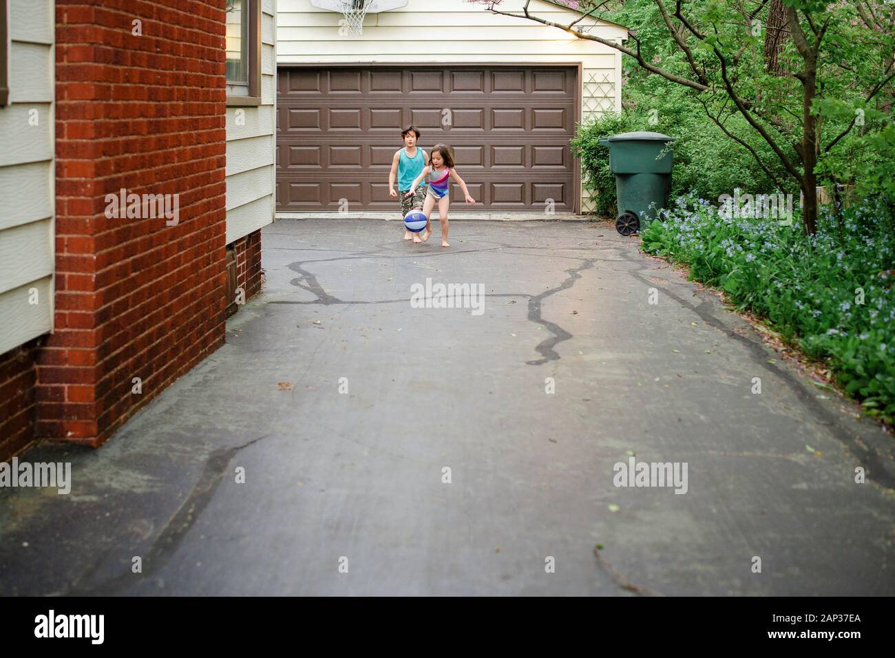 Un piccolo ragazzo e una ragazza giocano a basket insieme nel vialetto, a piedi nudi Foto Stock