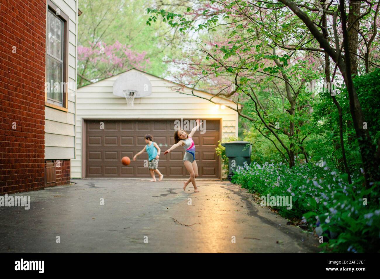 Una bambina balla a piedi nudi mentre il fratello gioca a basket sul retro Foto Stock