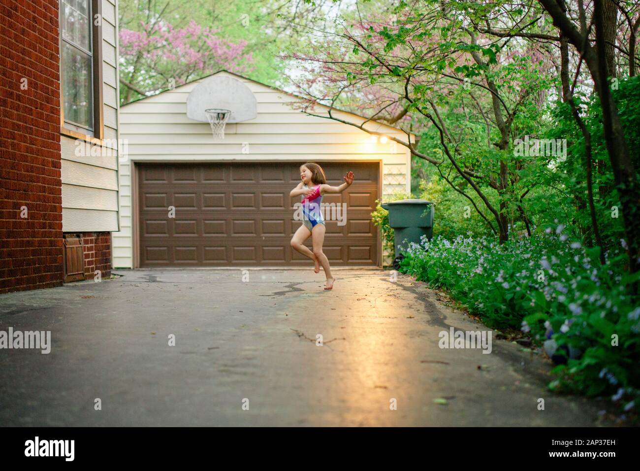 Una bambina balla felicemente a piedi nudi in una leotard nel suo viale d'accesso Foto Stock