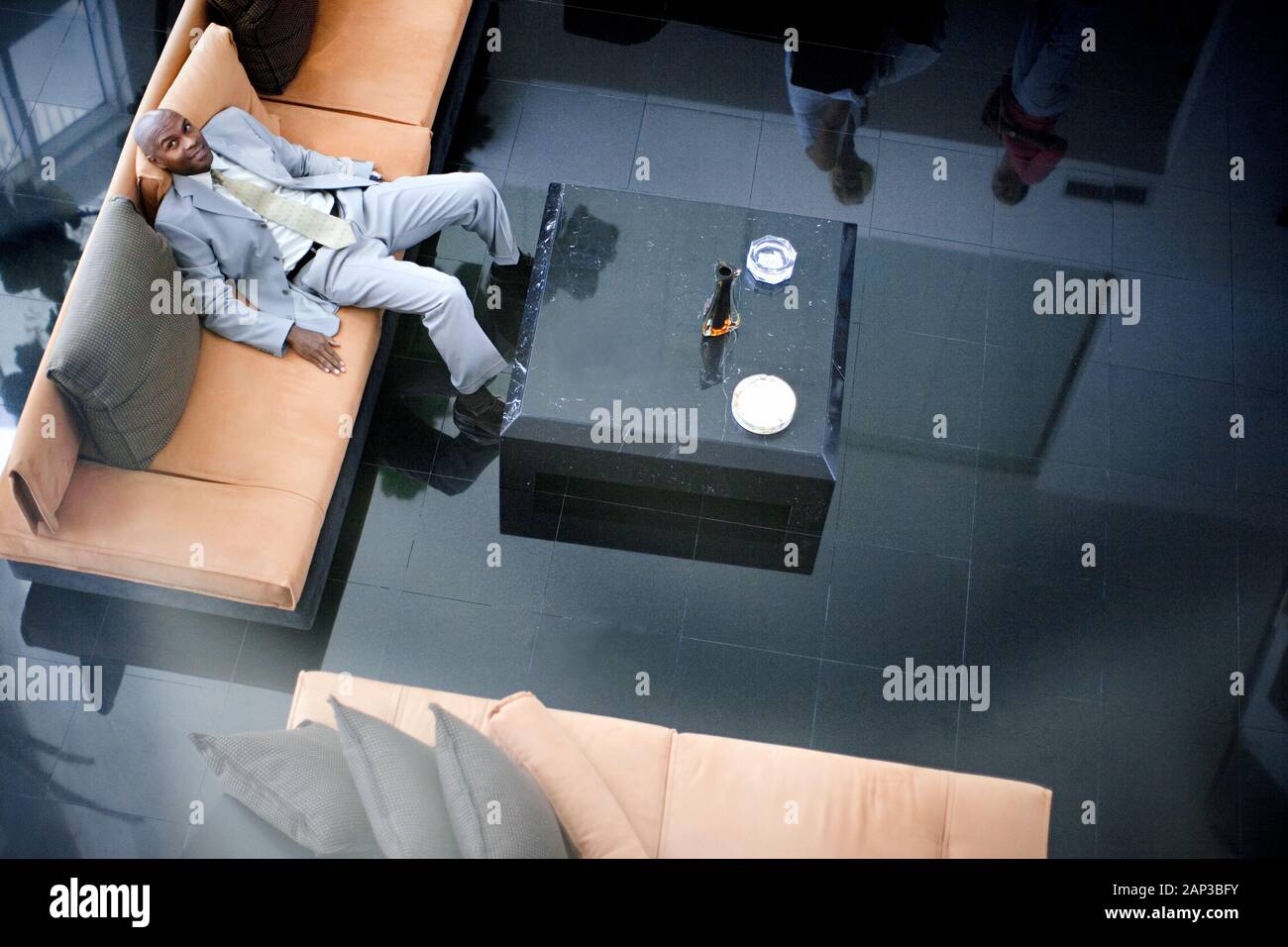 Sorridente mid-adulto uomo d affari slouching su un lettino all'interno di un ufficio lobby. Foto Stock