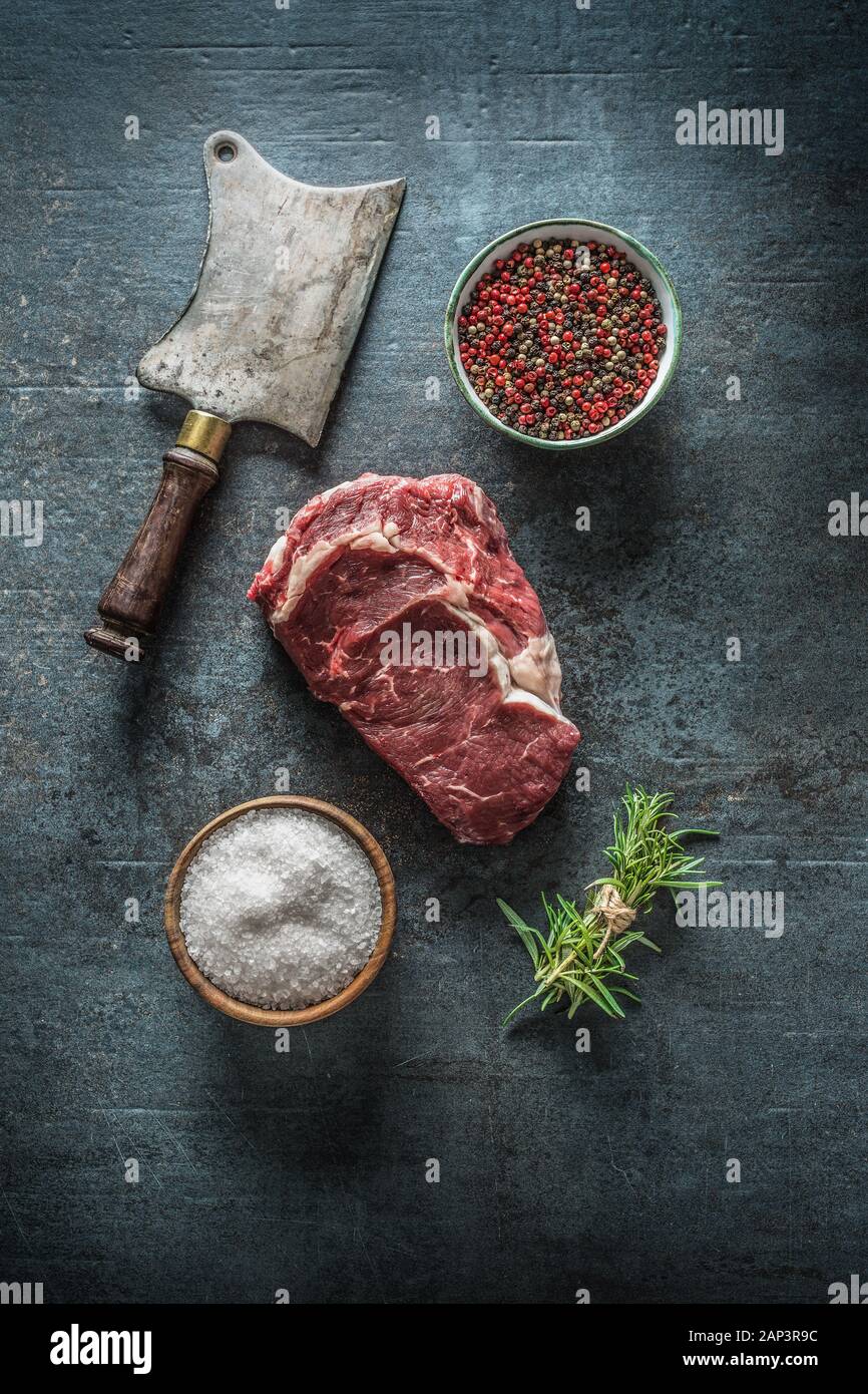 Raw bistecche di manzo con carne cleaver e sale pepe su scuro dello sfondo in calcestruzzo Foto Stock