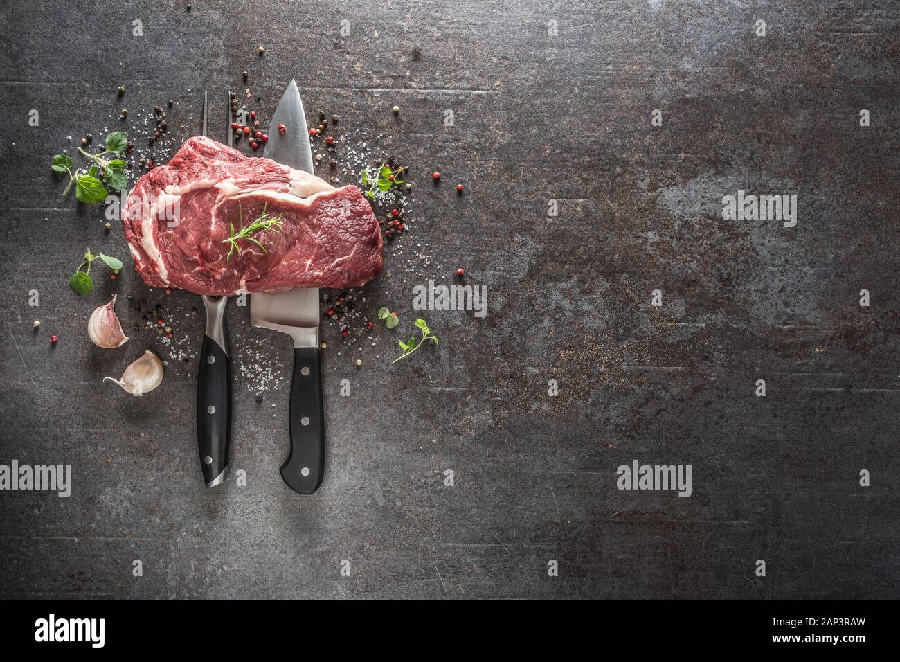 Materie bistecca con coltello e forchetta sale pepe e erbe su scuro dello sfondo in calcestruzzo Foto Stock