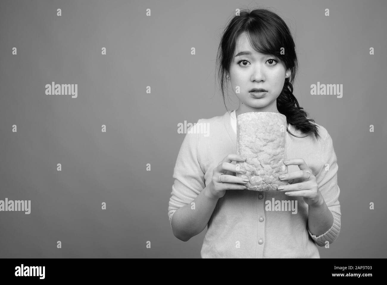 Giovane bella donna asiatica che tiene il pane su sfondo grigio Foto Stock