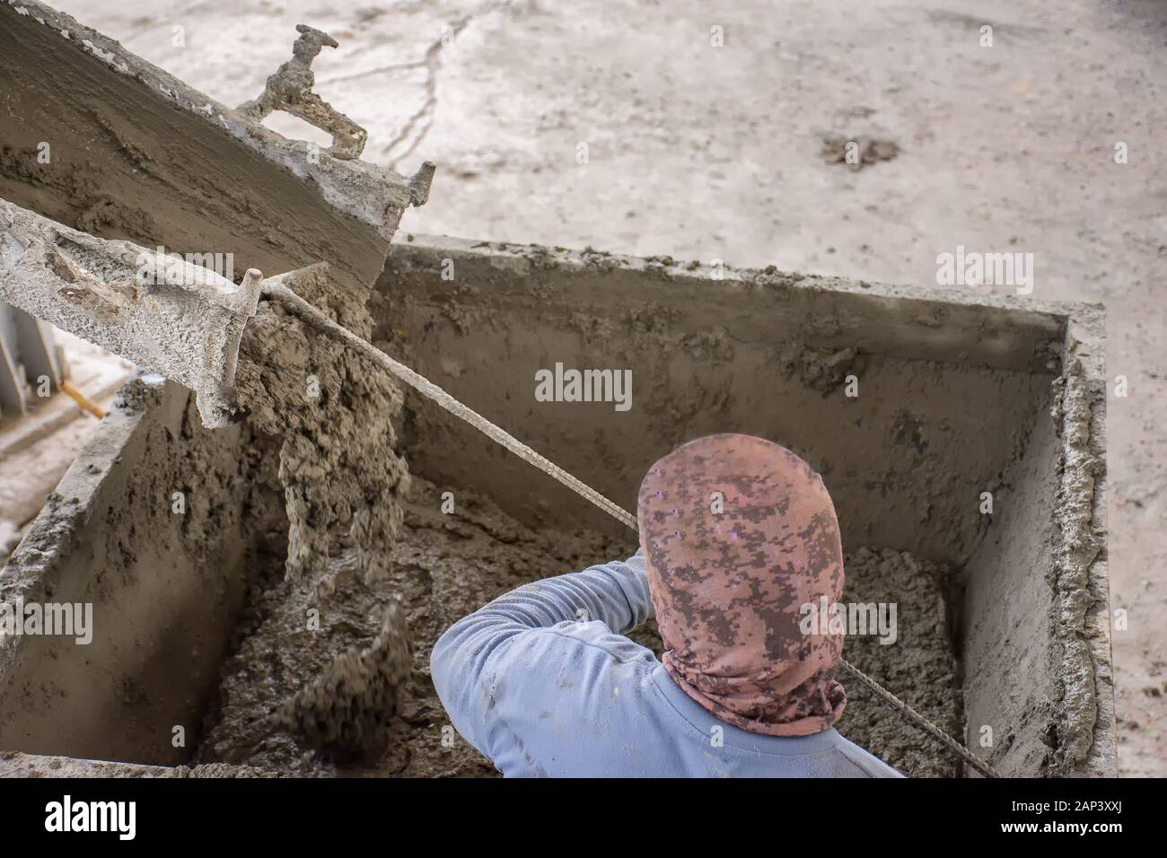 Lavoratore pala l'ultimo umido mix di cemento colata di cemento carrello scivolo nella benna di metallo a prepararsi per un altro processo. Foto Stock