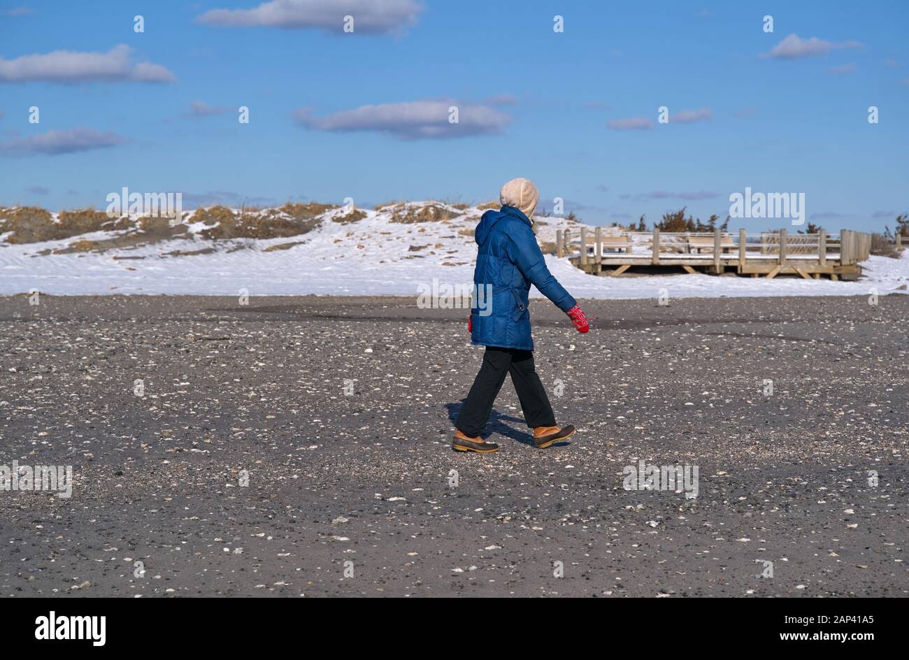 Signora anziana con abbigliamento freddo a piedi in spiaggia durante una stagione invernale del New England. Foto Stock