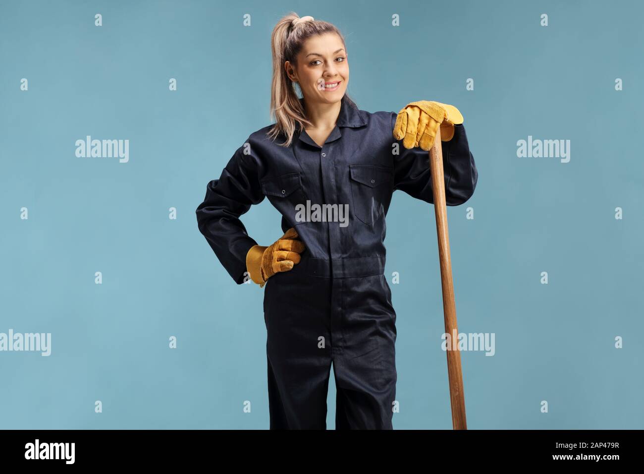 L'agricoltore femmina in un uniforme appoggiato su di un utensile di lavoro isolate su sfondo blu Foto Stock