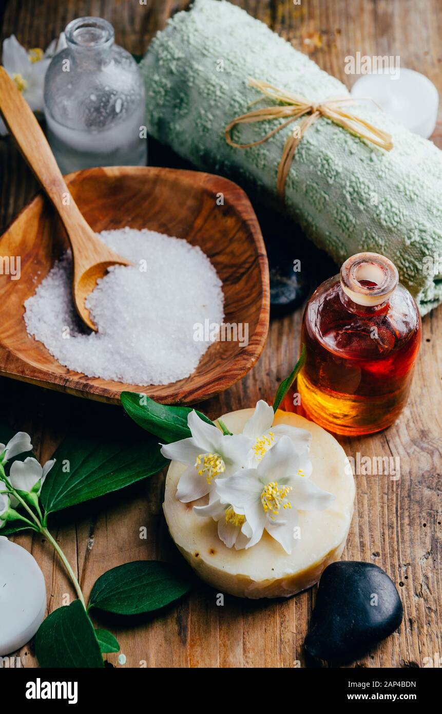 Cosmetici naturali spa con oli essenziali per massaggi, petali di fiori di gelsomino, pietra zen su sfondo rustico in legno. Sapone fatto a mano e aromaterapia alle erbe Foto Stock