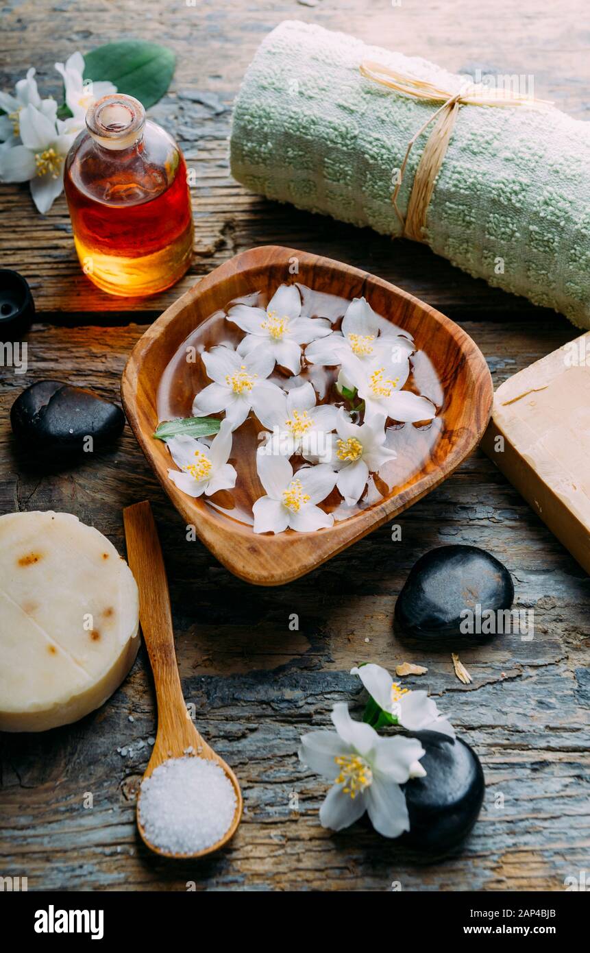 Cosmetici naturali spa con oli essenziali per massaggi, petali di fiori di gelsomino, pietra zen su sfondo rustico in legno. Sapone fatto a mano e aromaterapia alle erbe Foto Stock