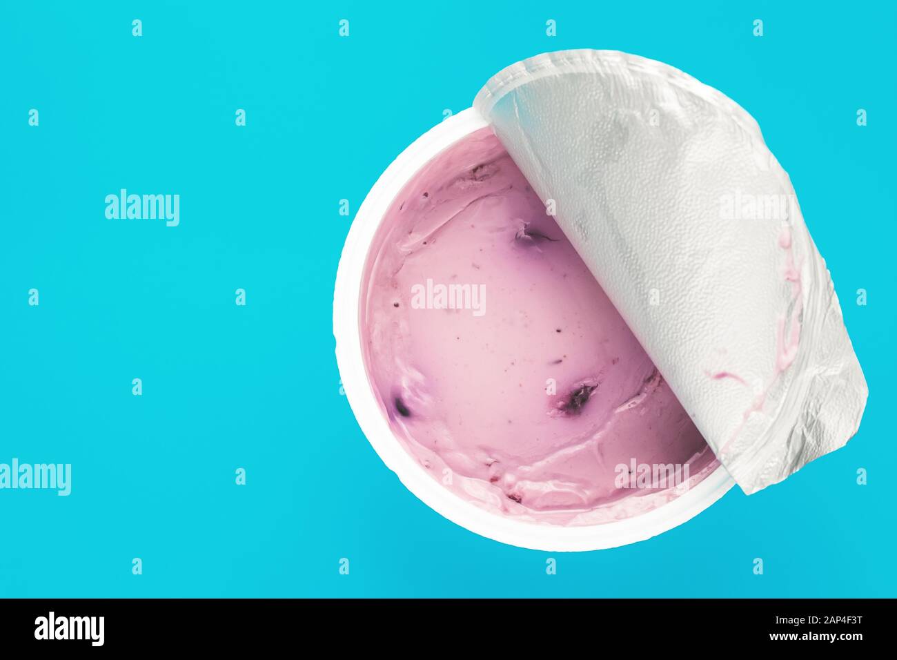 Uno yogurt rosa con mirtillo in una tazza di plastica aperta su sfondo blu. Vista dall'alto, spazio di testo Foto Stock